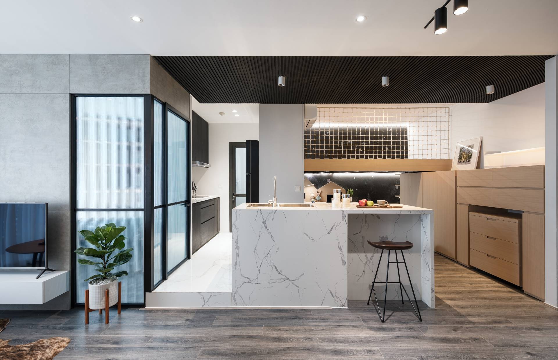 The kitchen area is airy. Its floor is raised up. The stone material is used in sync with the bar, both helping to divide and create a connection between spaces.