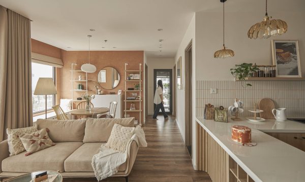 Neutral fabric sofa, decorated with a Scandinavian brocade patterned pillow. Behind is the dining area with decorative shelves.