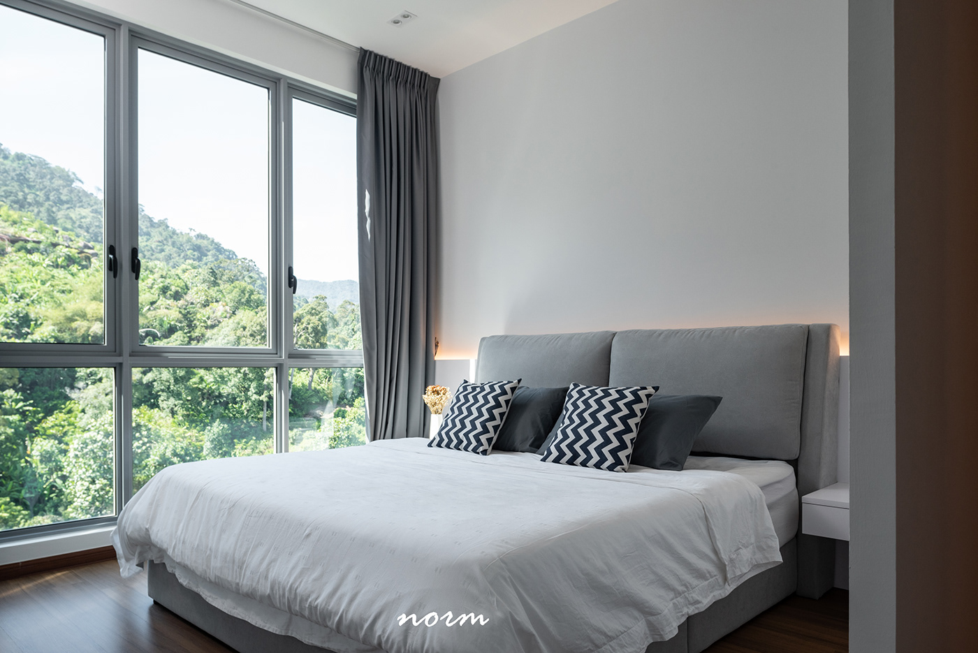 Master bedroom has a simple mattress bed and is filled with natural light from the floor-to-ceiling window. Main colors, such as gray and white combined with the scenery outside the window evoke feelings of closeness, comfort, as well as relaxation. 